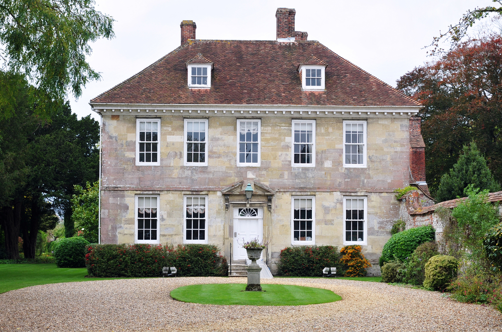 A three-story house of gray stone, with a round drive in front of it for carriages, and large glass windows in front.