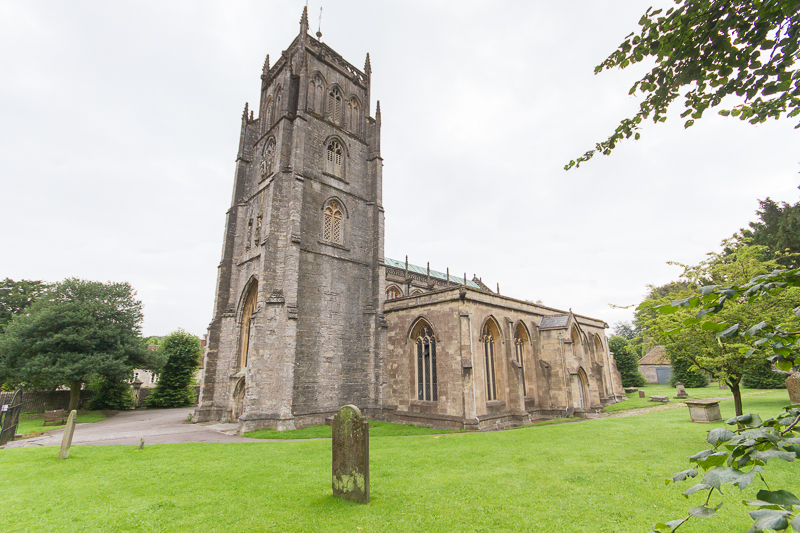 A stone church on a grass green, tower high in the foreground