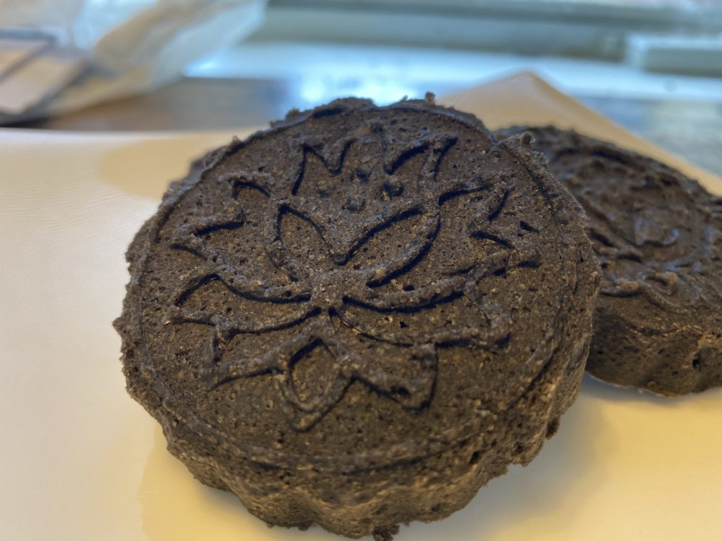 20BCB6F0-9433-4E5A-8F75-5FCF845B8209 round black sesame cake with a lotus molded on the top.
