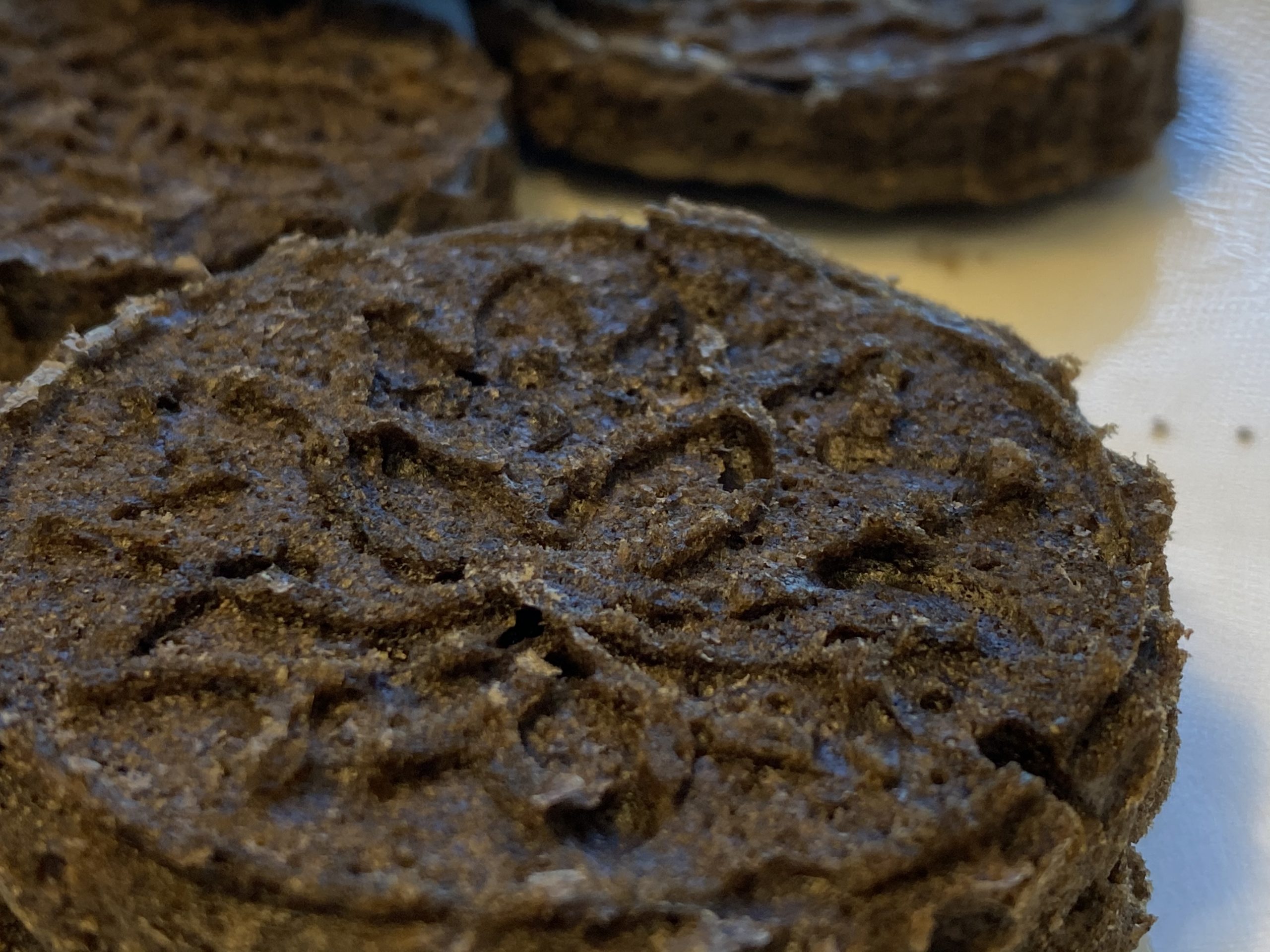 5C8505B7-E9F7-435B-948C-51B45AF83FBC Picture of black sesame pound cake: round dark brown cakes with a delicate lotus pattern stamped on top.