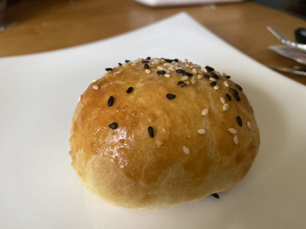 A beautiful baked bao, golden yellow, with black and white sesame seeds on top